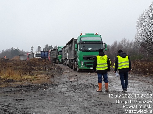 Inspektorzy Wojewódzkiego Inspektoratu Ochrony Środowiska w Warszawie stojący przed kolumną samochodów ciężarowych nielegalnie transportujących odpady.
