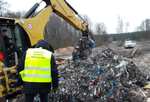 Inspektor Wojewódzkiego Inspektoratu Ochrony Środowiska w Warszawie stoi przy koparce przekopującej nielegalnie zgromadzone odpady.